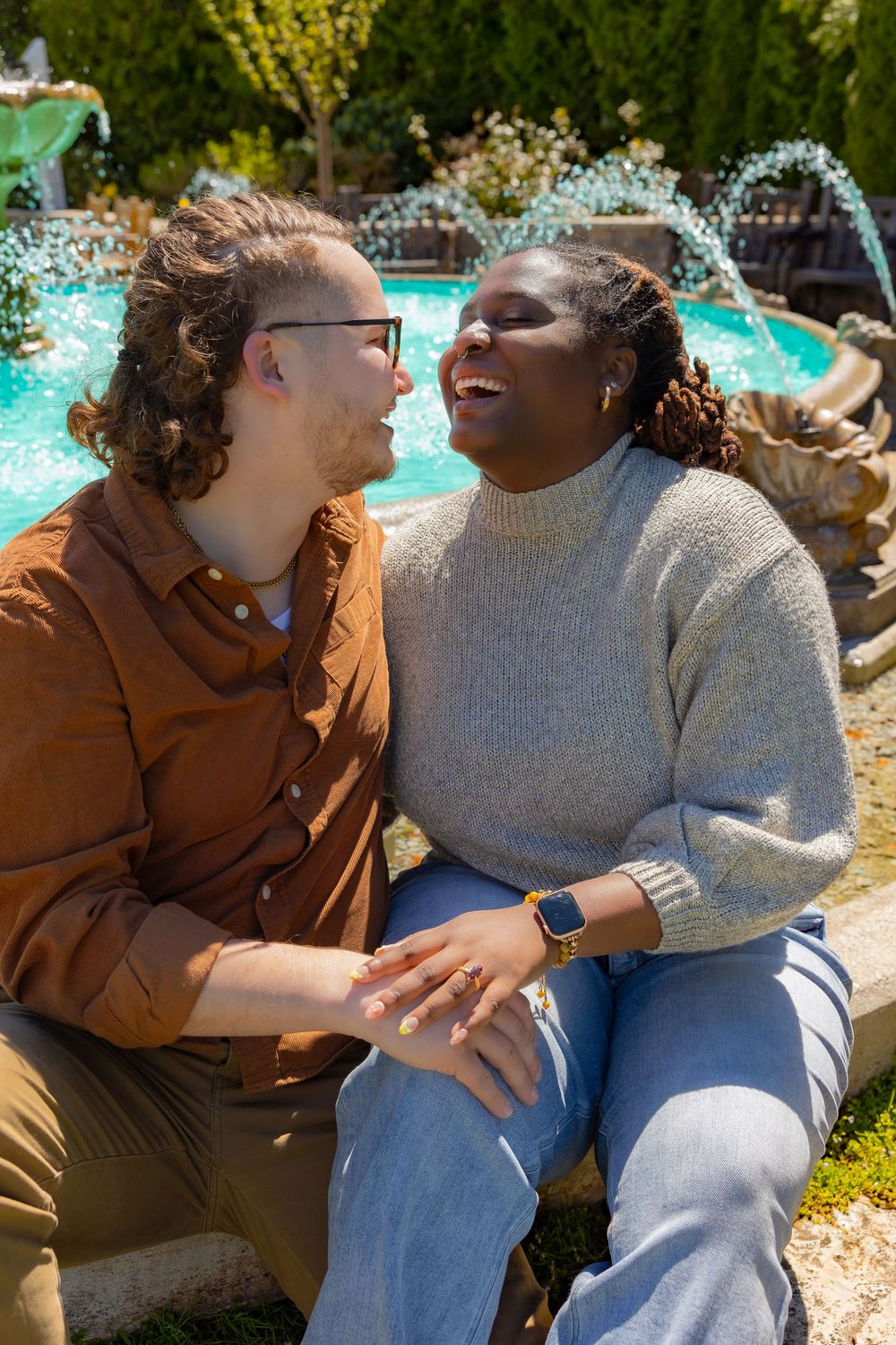 Two people share a joyful moment while sitting together outdoors on a sunny day.