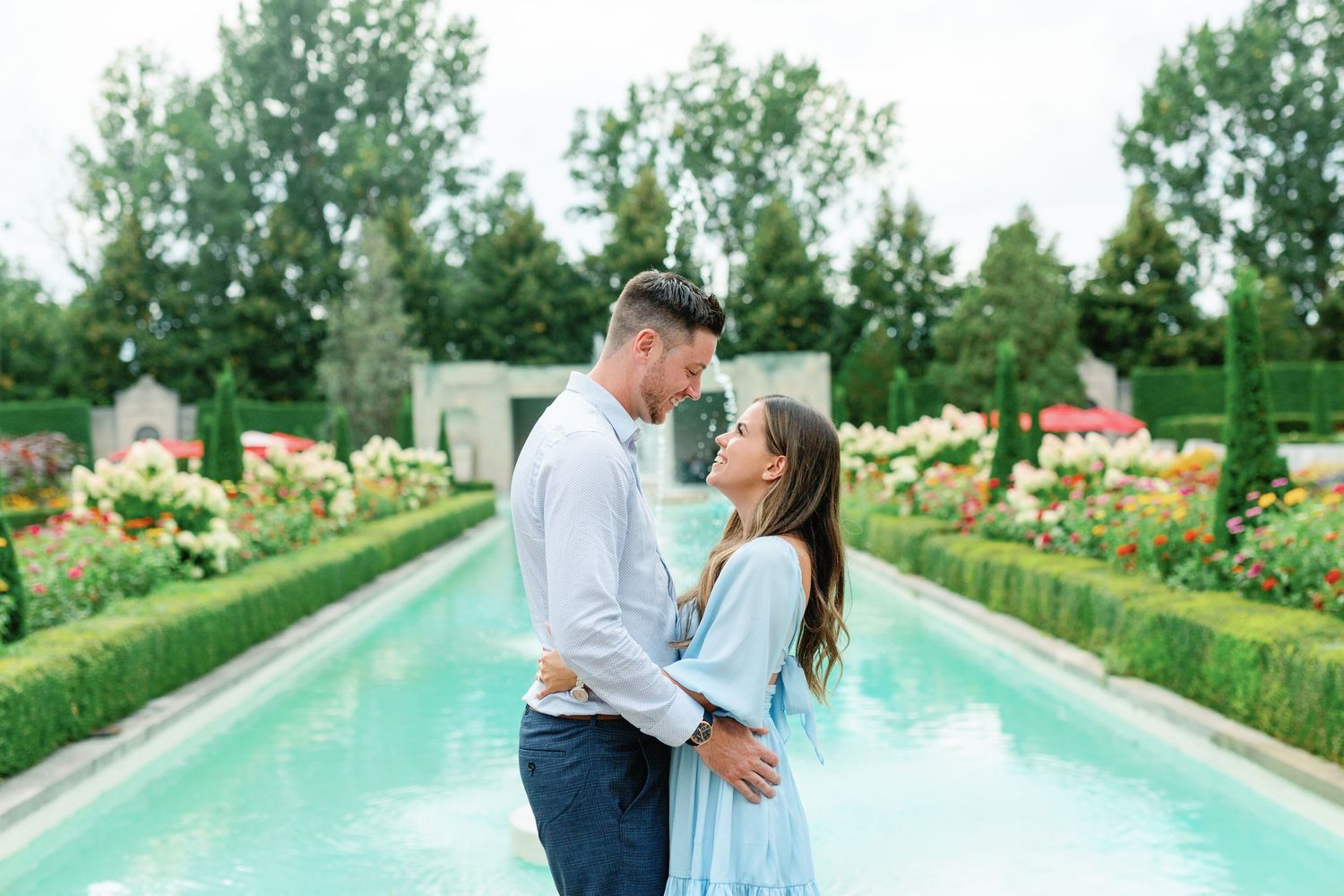 Romantic couple photoshoot by a serene swimming pool surrounded by manicured gardens.