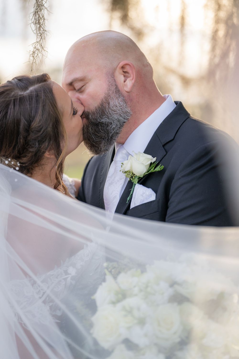 A tender wedding kiss captured between newlyweds amid soft lighting and flowing white veil.