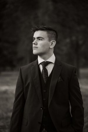 Black and white portrait of a young person in a formal three-piece suit with tie looking off to the side thoughtfully.