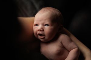 A newborn baby lies against a dark background with dramatic lighting creating a warm, intimate portrait.