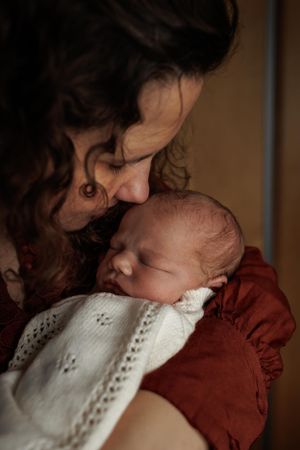 A tender moment captured between a parent and sleeping newborn baby wrapped in a white and red outfit.