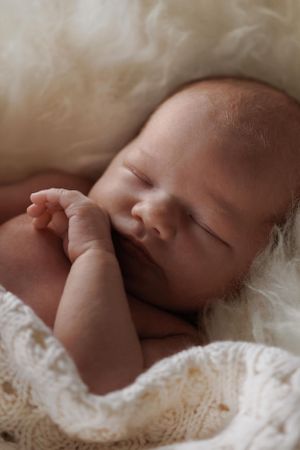 A sleeping baby wrapped in a white knitted blanket rests peacefully in soft natural lighting.