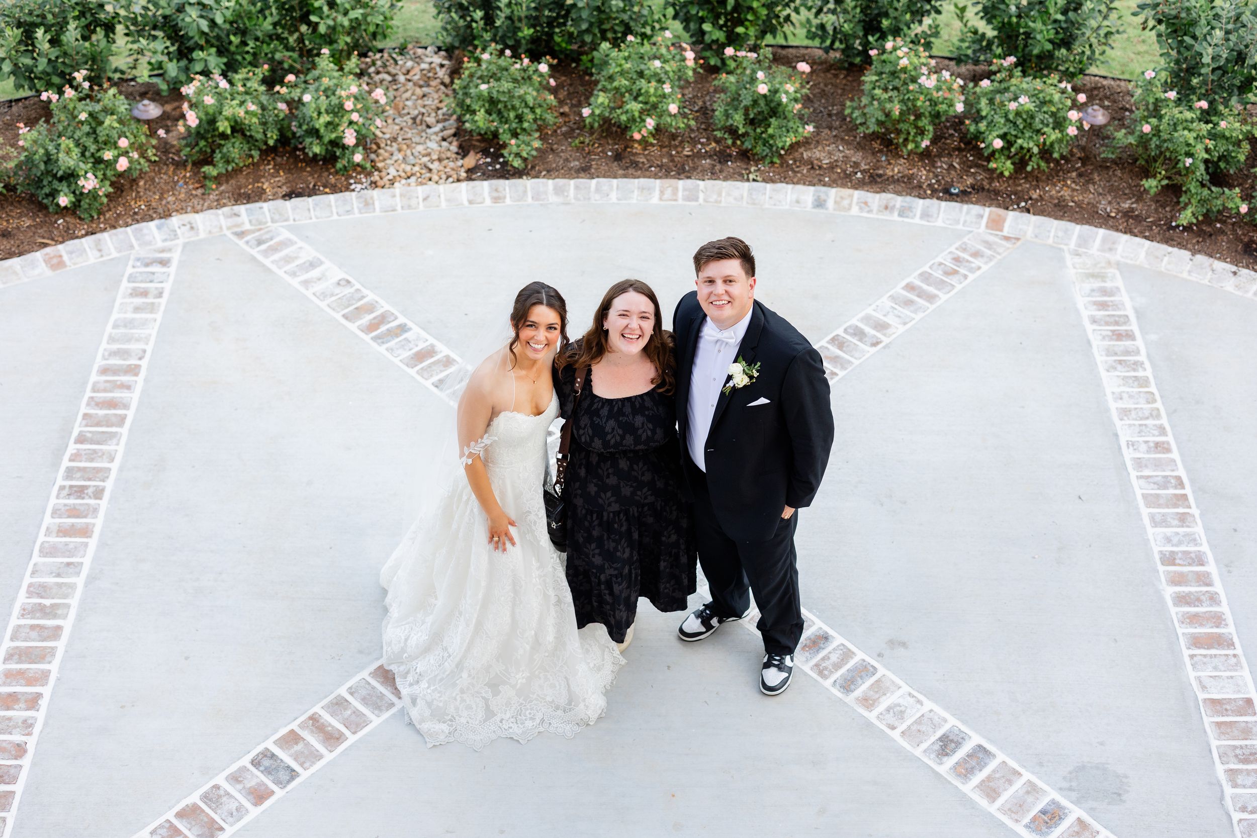 Three people stand together on a decorative brick paved patio surrounded by garden landscaping.