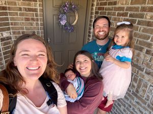 Smiling family of five gathered together on front porch with brick wall and lavender wreath on door.