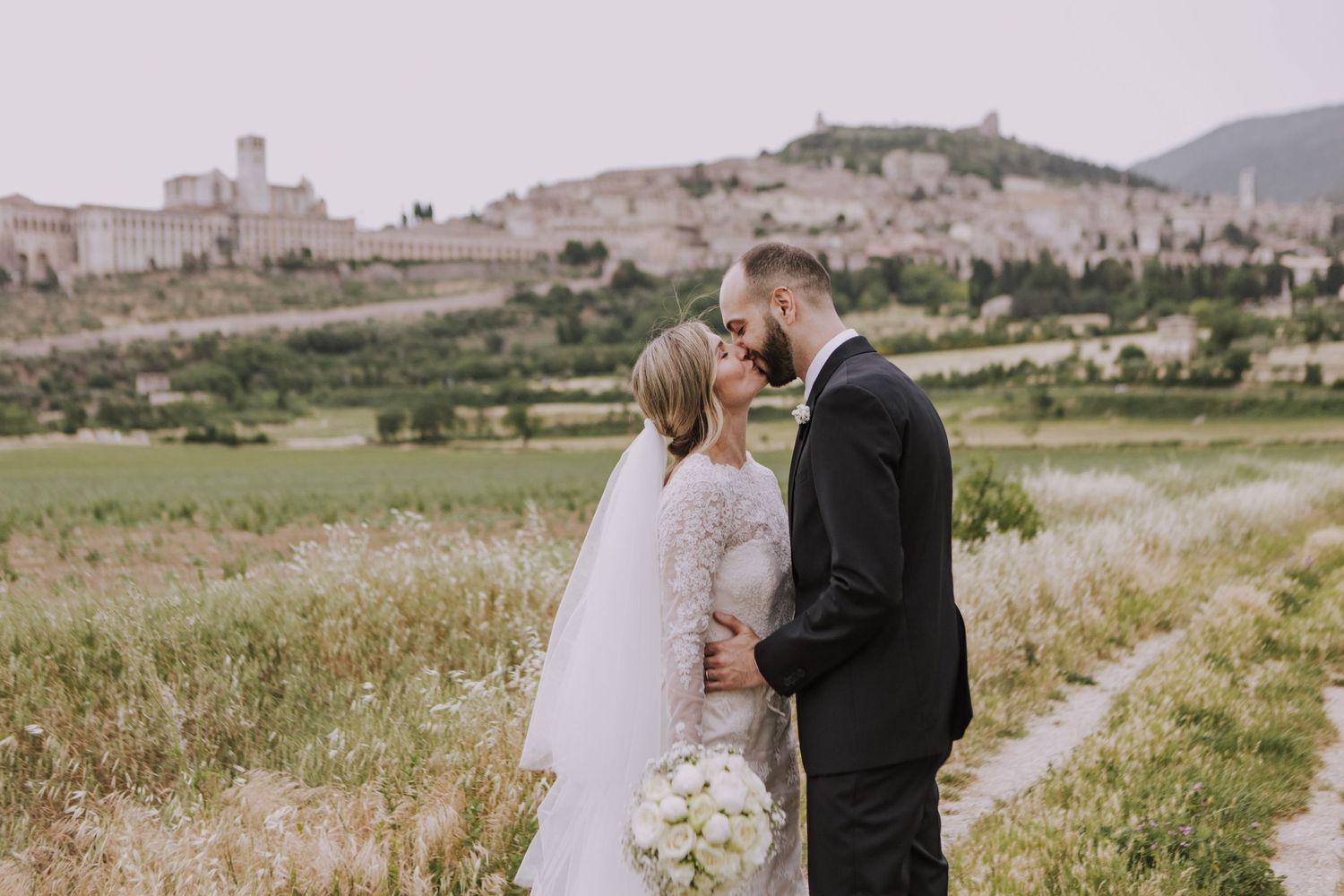A romantic wedding moment captured in an Italian countryside with ancient architecture in the distance.