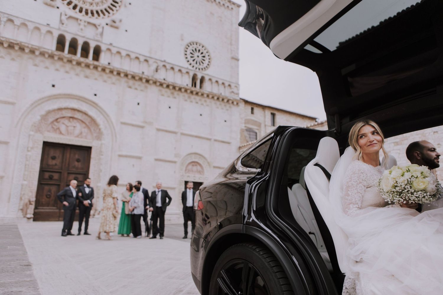 A bride exits a black car outside a historic Italian church with ornate architectural details.