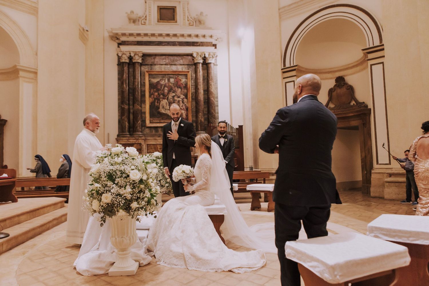 Wedding ceremony in an elegant church with ornate altar and floral decorations.