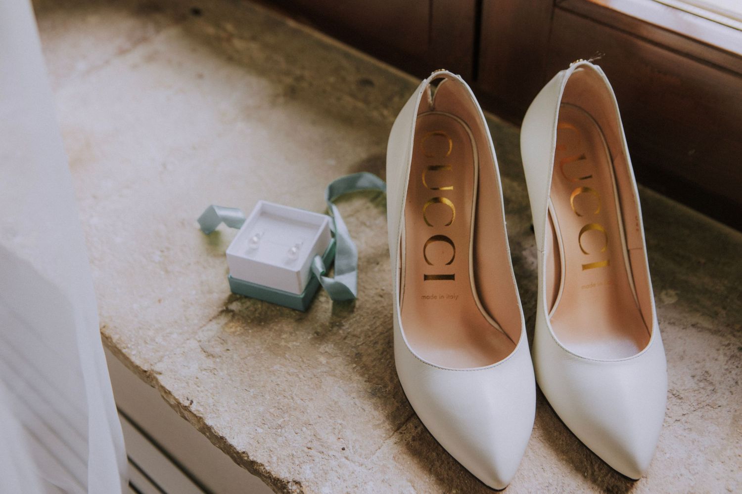 Elegant white bridal heels displayed on windowsill.