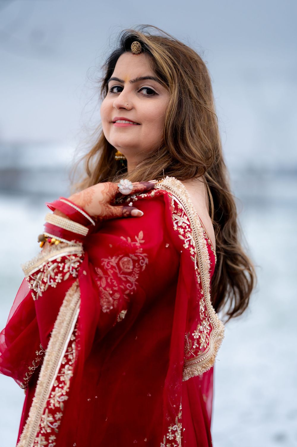 Woman in red embroidered Indian dress poses against snowy winter backdrop.