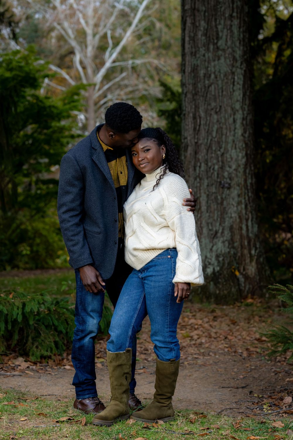 Couple in casual denim and sweaters sharing a tender moment in a forest setting.