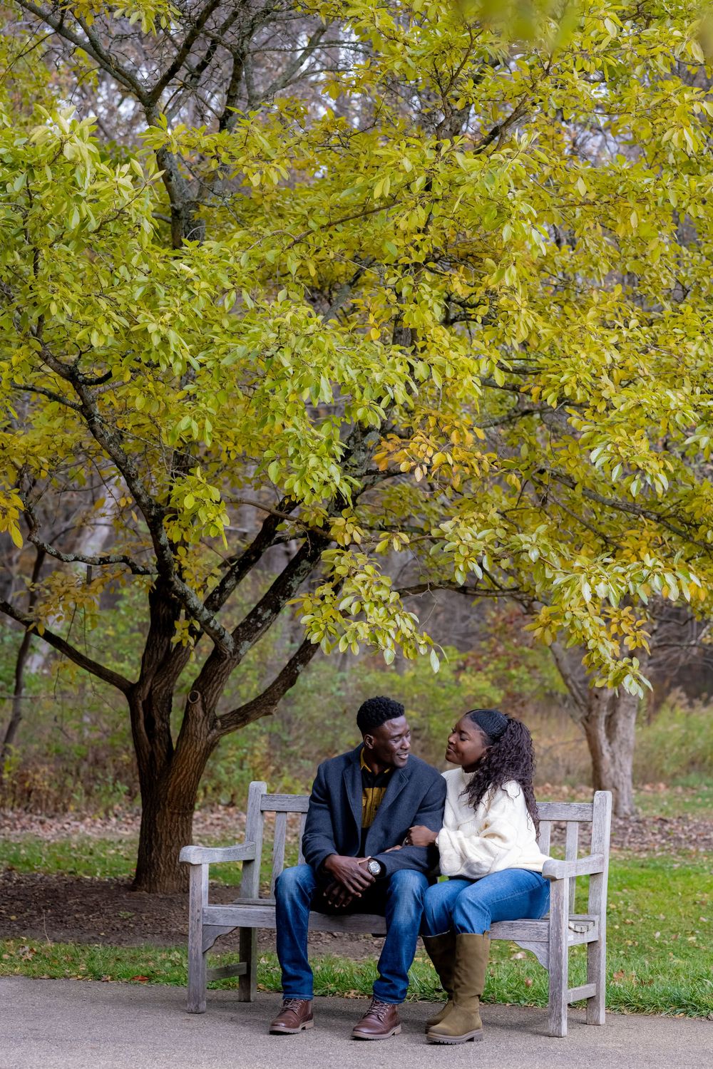 Couple sitting together on a white bench under yellow autumn trees in a park.