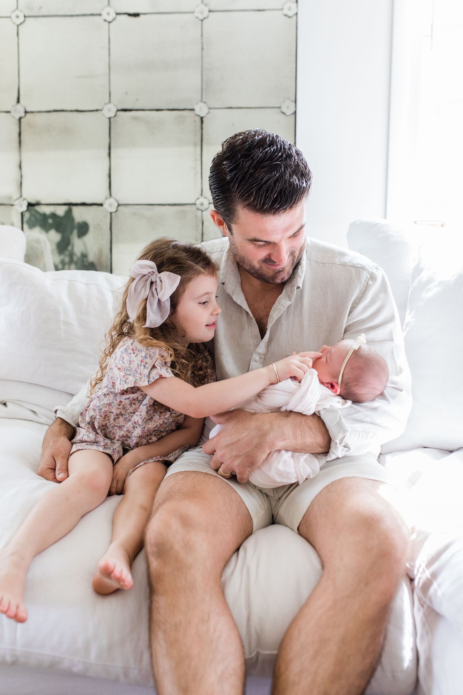 Tender family moments captured on white couch in bright minimalist setting.