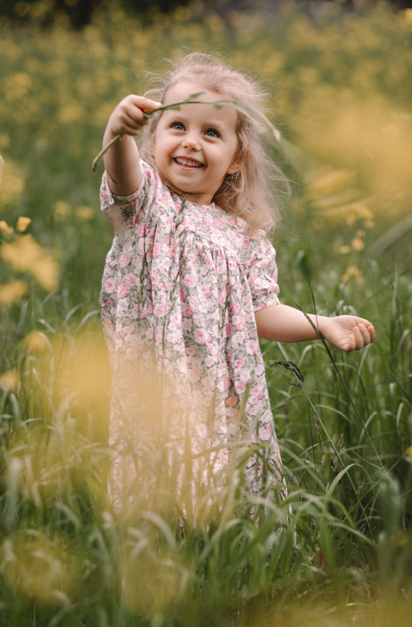 Child playing joyfully in tall grass wearing floral dress during golden hour.