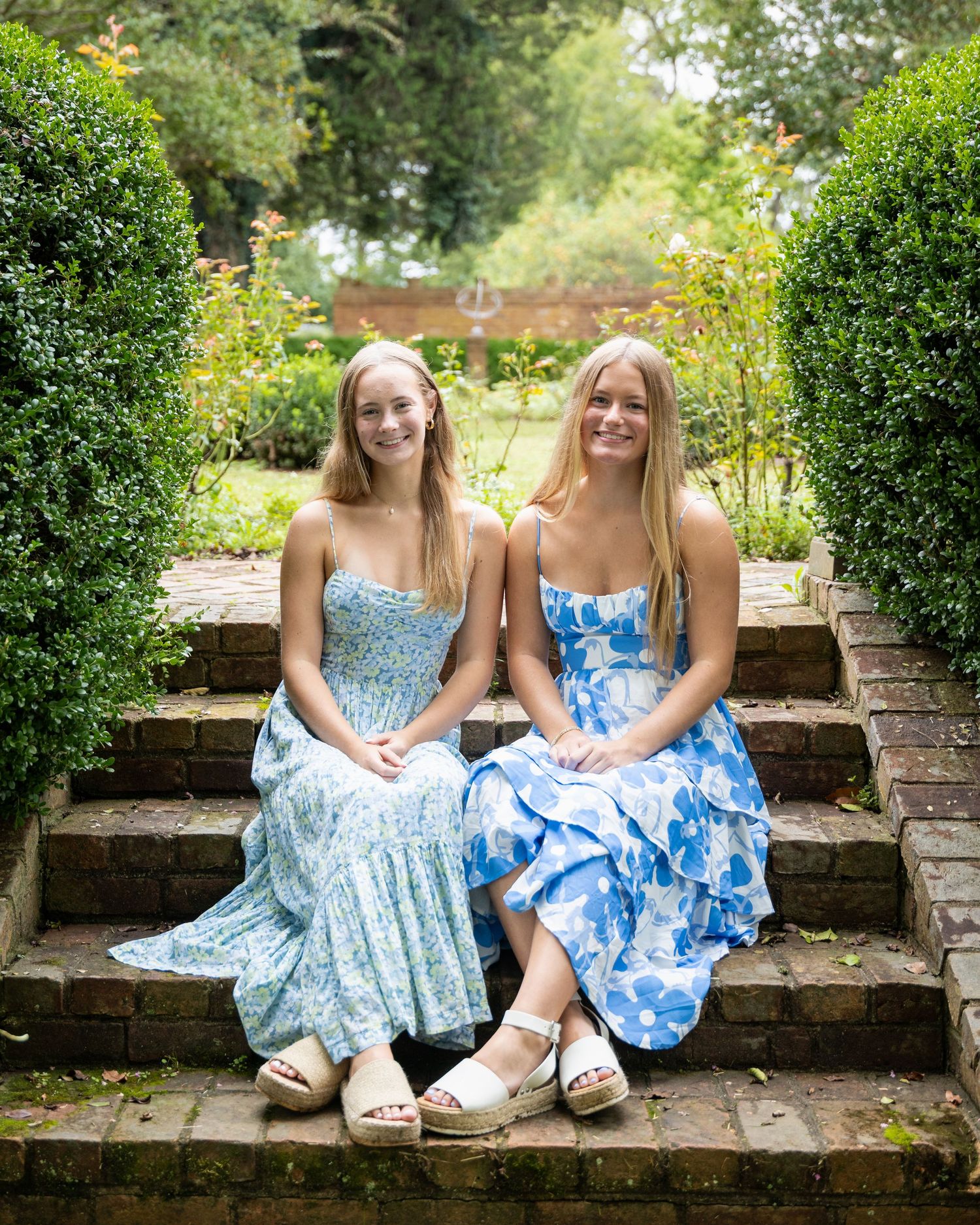 People wearing blue floral dresses sitting together on brick steps in garden setting.