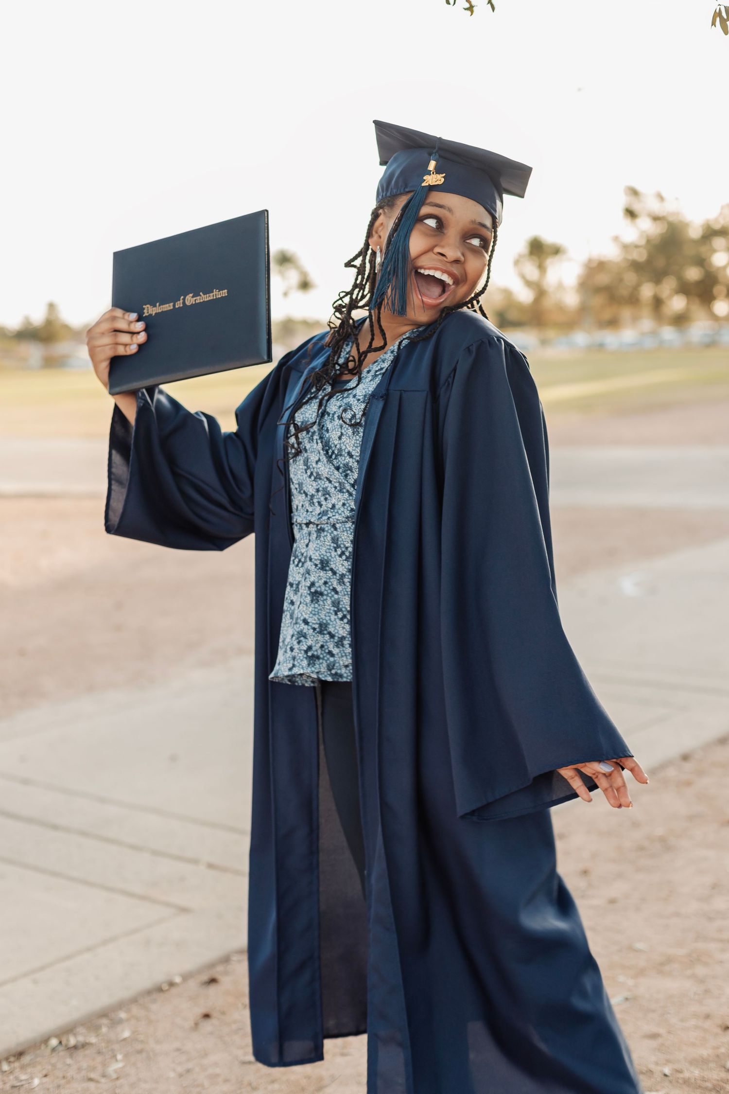 Joyful Black female graduate in navy cap and gown holding diploma outdoors, celebrating her achievement.