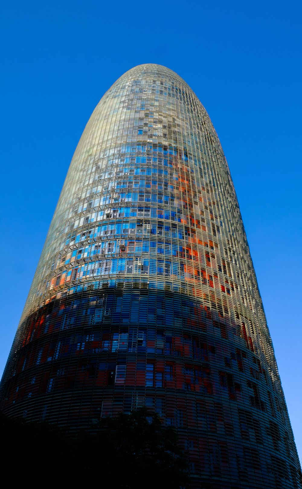 Futuristic Torre Agbar skyscraper with colorful glass facade rising against a clear blue sky in Barcelona, Spain.