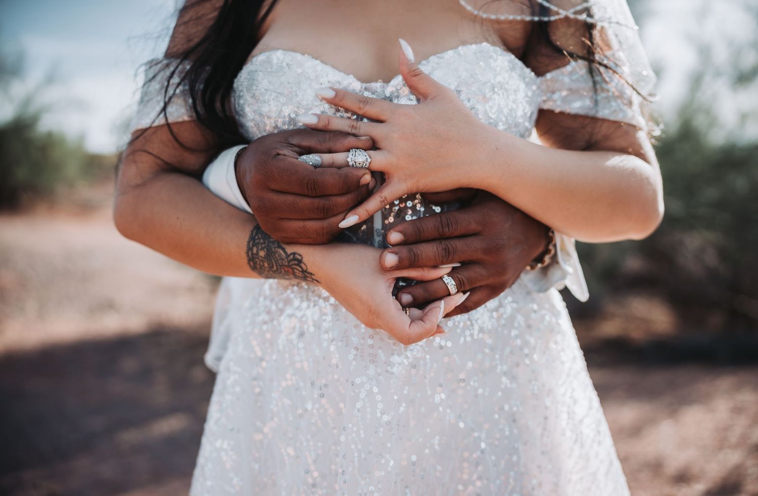 Close-up of hands wearing wedding dress and rings in desert setting.