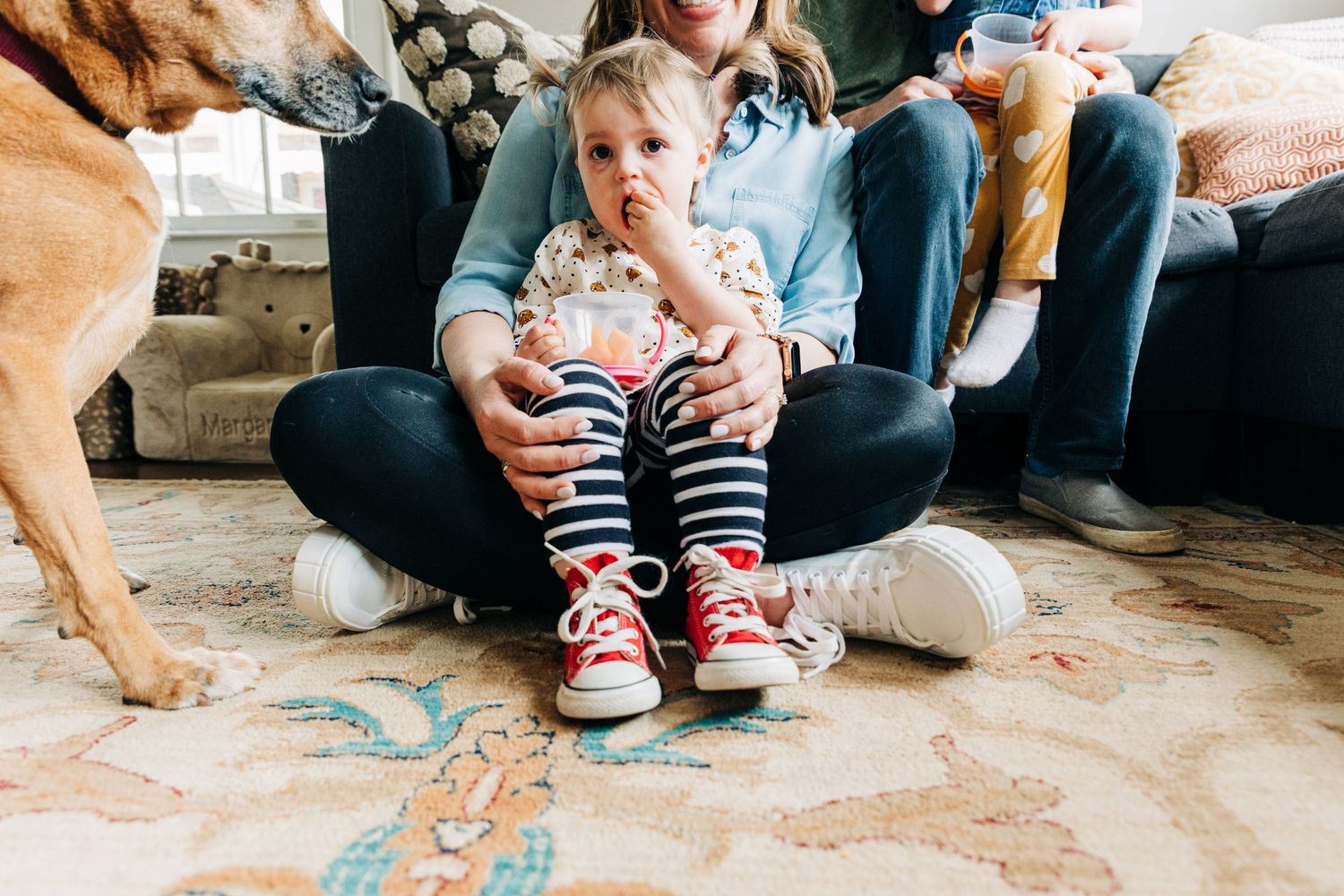 Little girl with a black eye and striped pants eats goldfish on her mom's lap