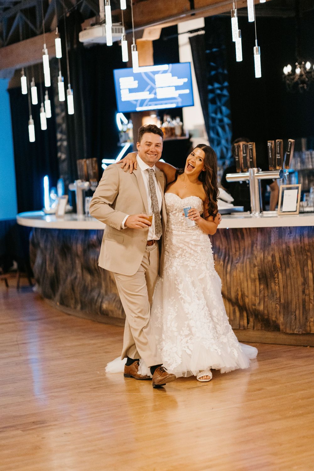 Smiling bride and groom pose together near bar at elegant wedding reception venue.