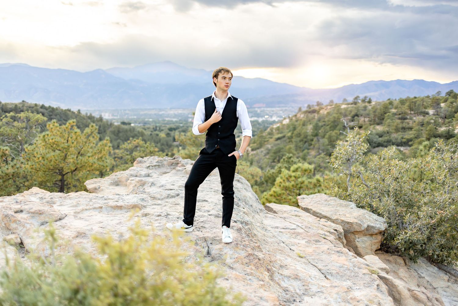 Senior guy poses on the rocks at sunset and gazes into the distance at his senior session at Palmer Park in Colorado Spr
