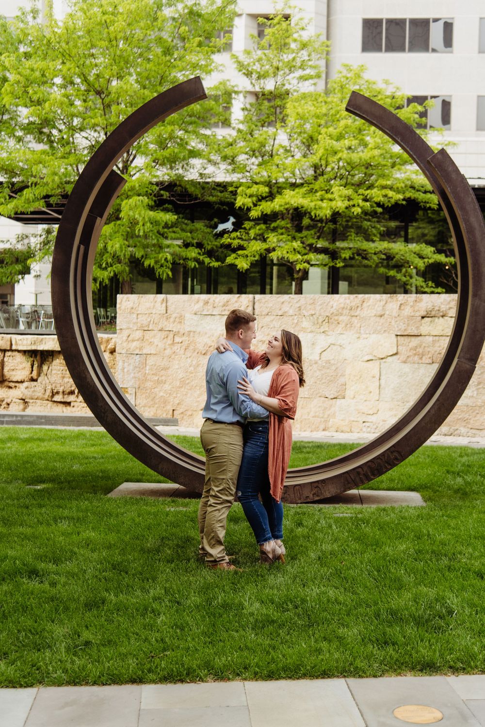 Romantic couple shares tender moments through a large circular art installation in a park setting.