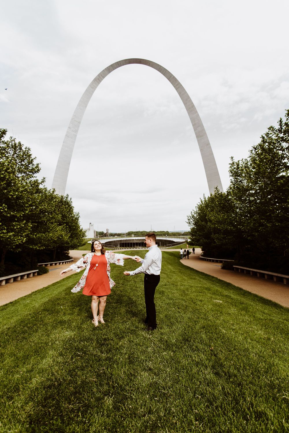 Romantic moments captured under the Gateway Arch with cloudy sky backdrop.