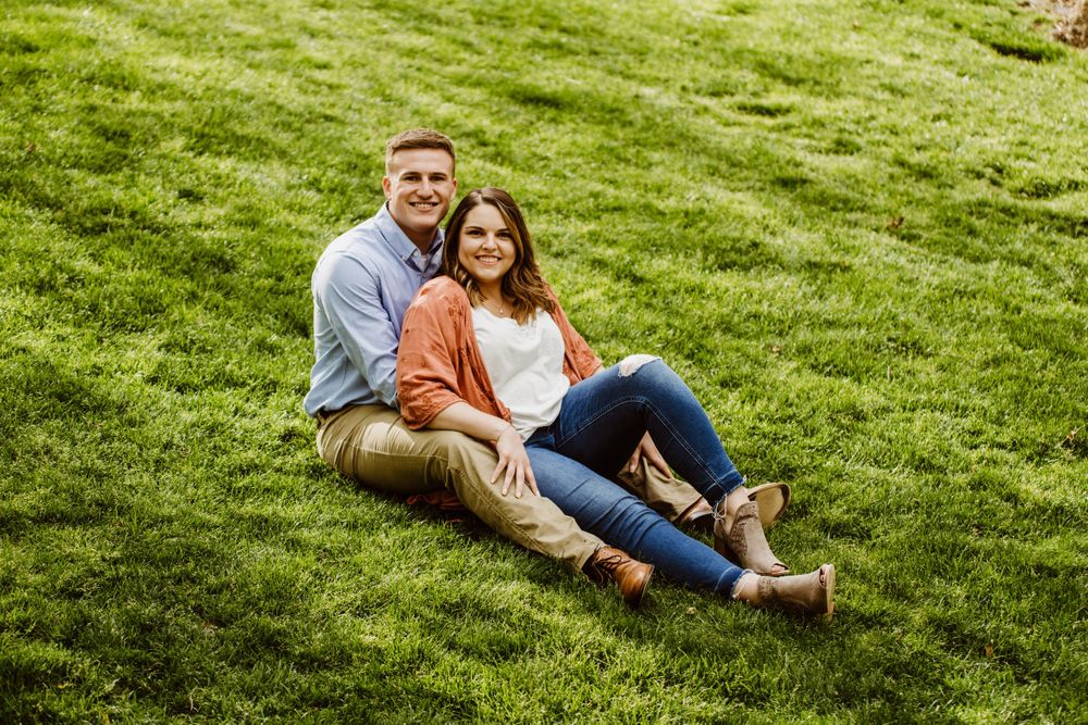 A couple lounges casually on a grassy hillside during a summer day.