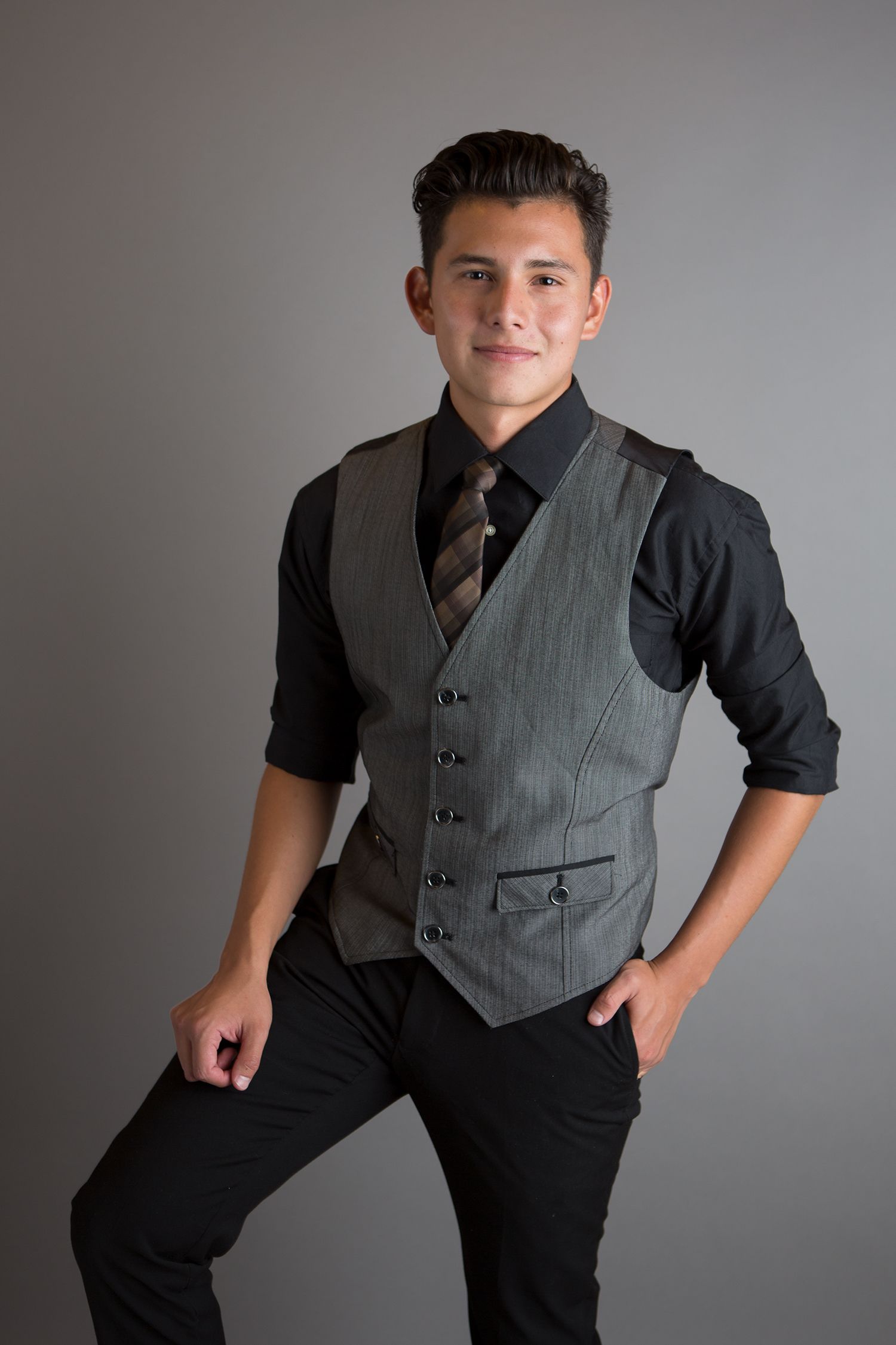 Young person in gray vest and black shirt posing against gray background.