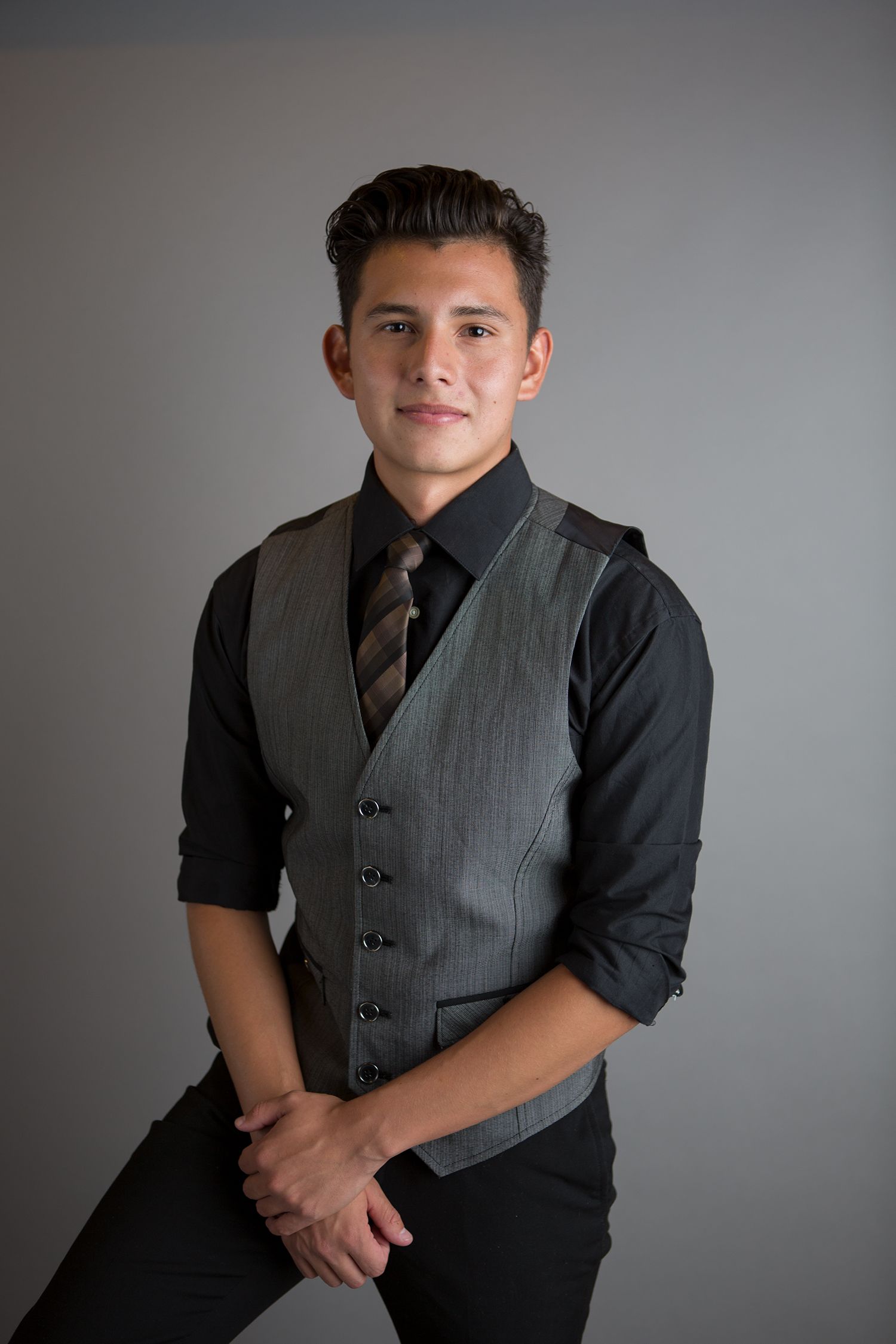Studio portrait with person in business casual attire against gray backdrop.