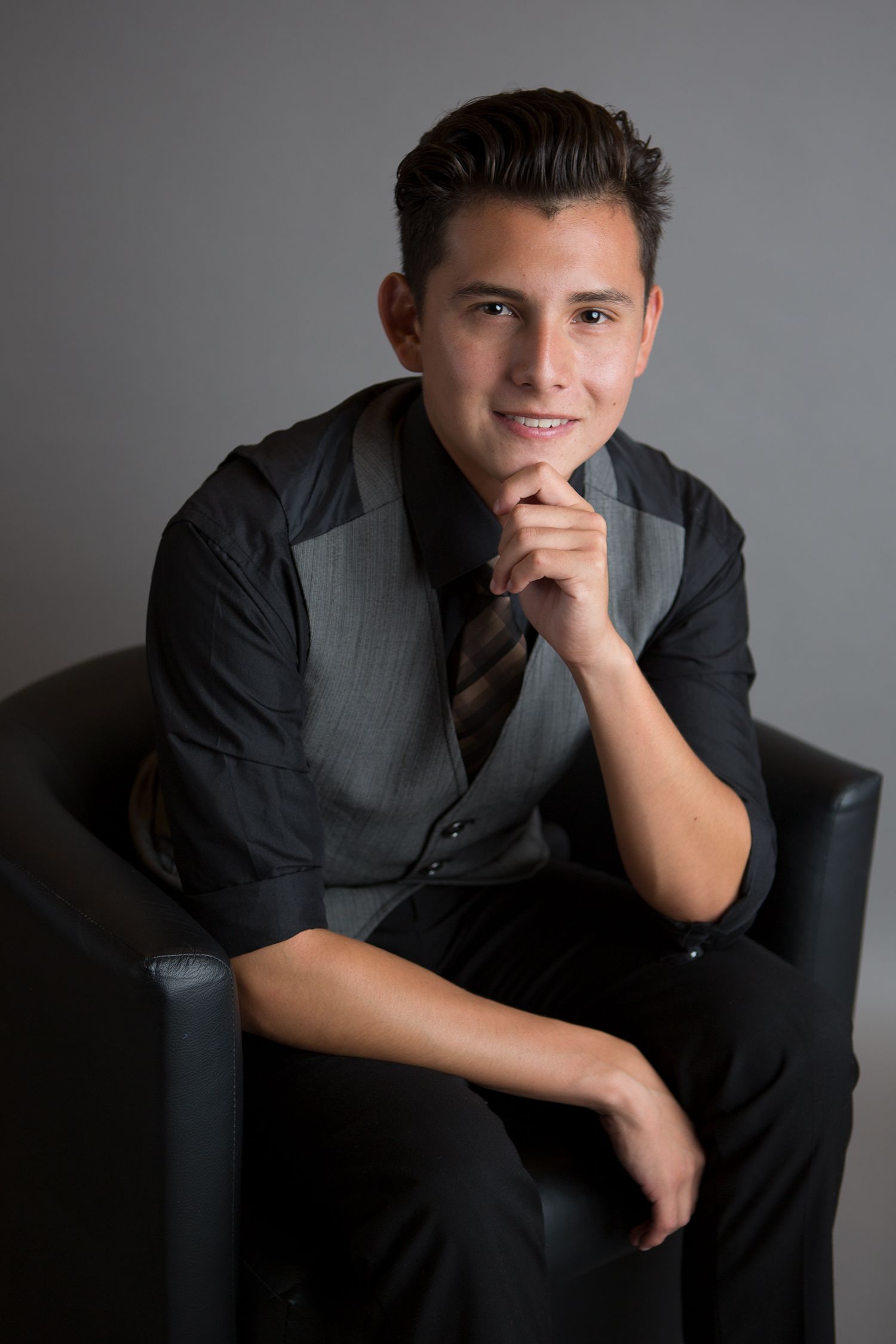 Person in vest and dress shirt seated thoughtfully in studio setting.