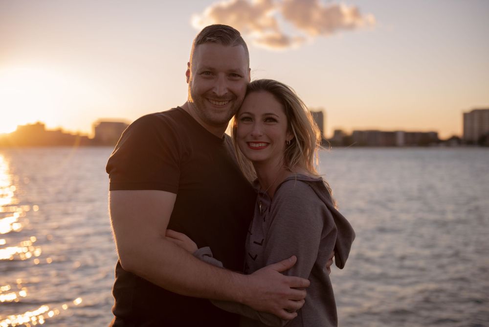 Romantic sunset portrait of a couple embracing by the waterfront with city skyline in background.