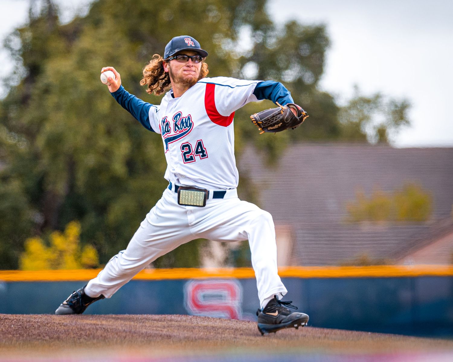 Baseball pitcher in white uniform delivers pitch from mound during game.