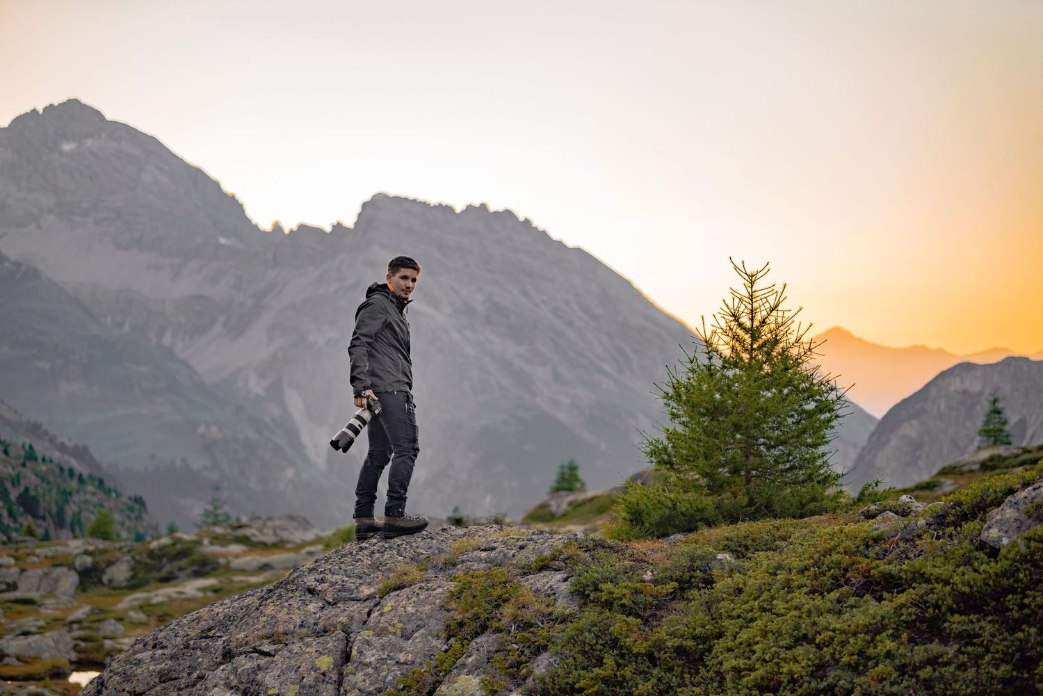 Silhouette of photographer standing on rocky mountain peak during golden sunset.