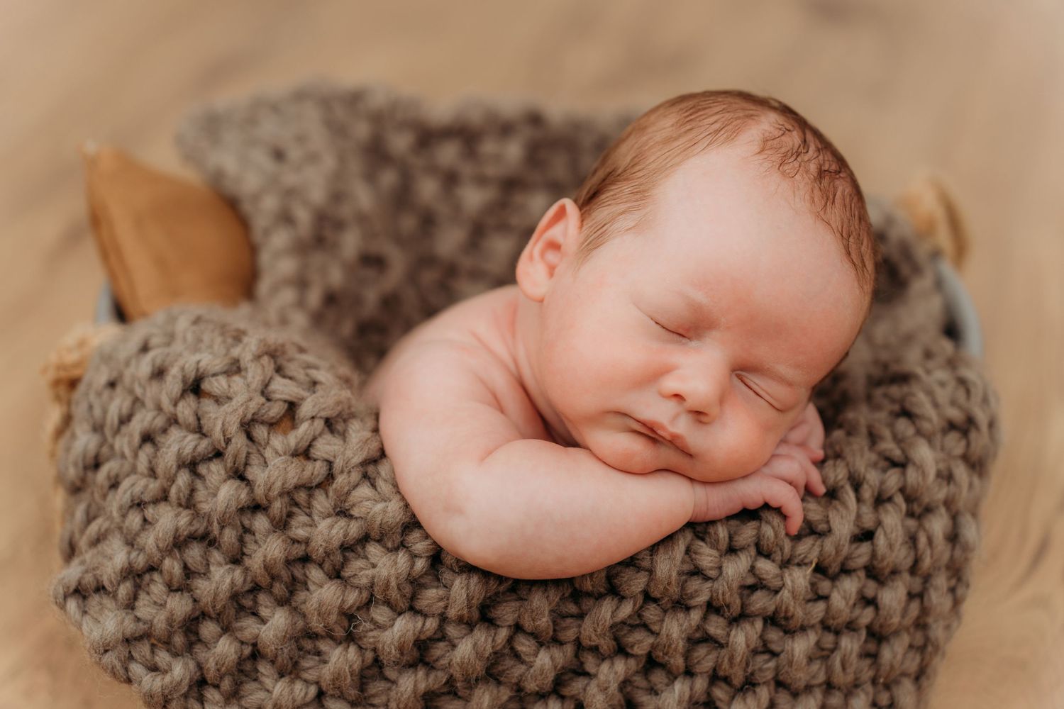 Sleeping newborn peacefully resting on chunky knit gray blanket during professional photo session.