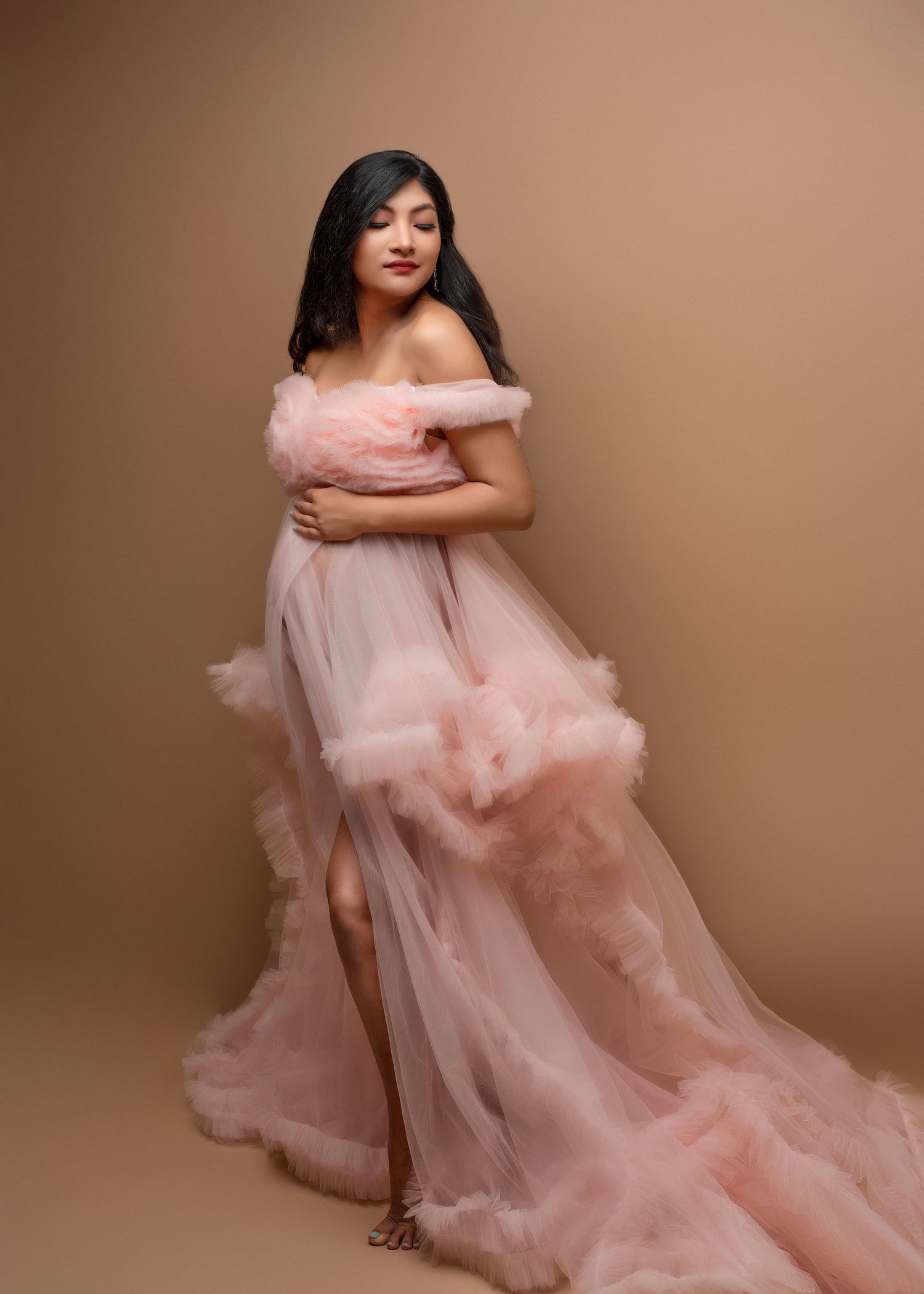 an expecting mother smiles over her shoulder in a cotton candy pink dress in a photo studio