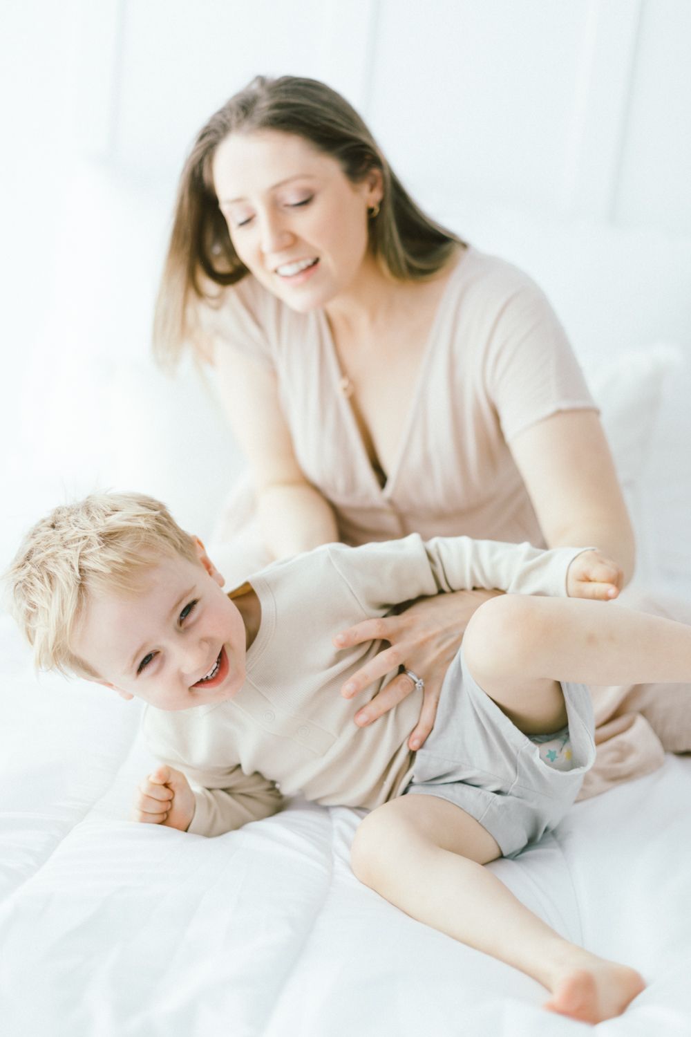 Joyful playtime between parent and child on white bedding.