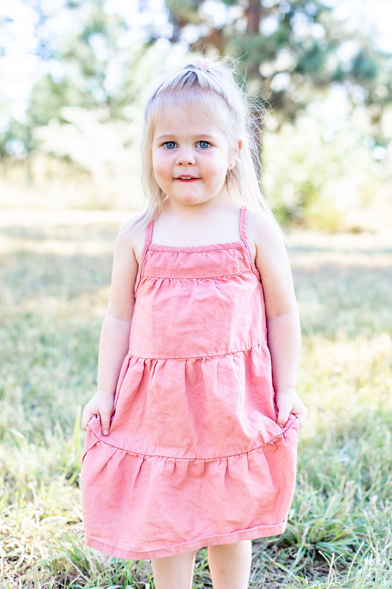 toddler girl holds her pink dress and smiles in Black Forest, Colorado.