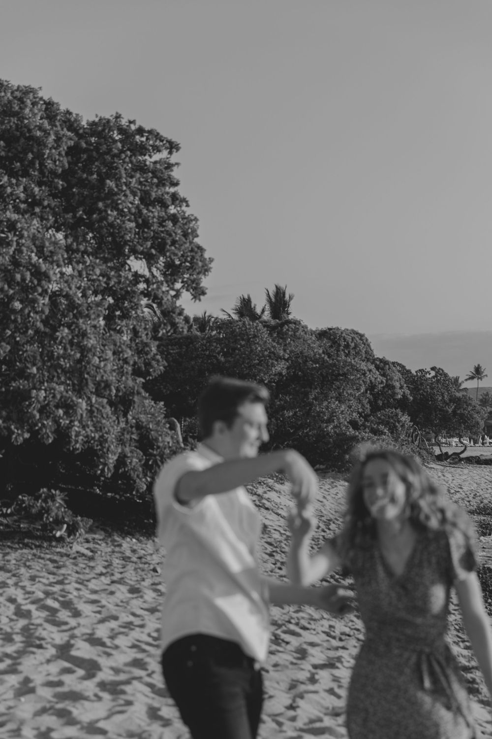 A couple dances joyfully together on a sandy beach at sunset.