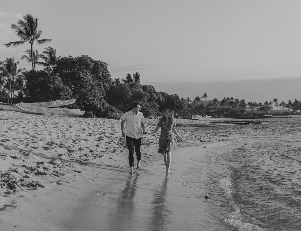 A romantic black and white photo of a couple walking together on a tropical beach.