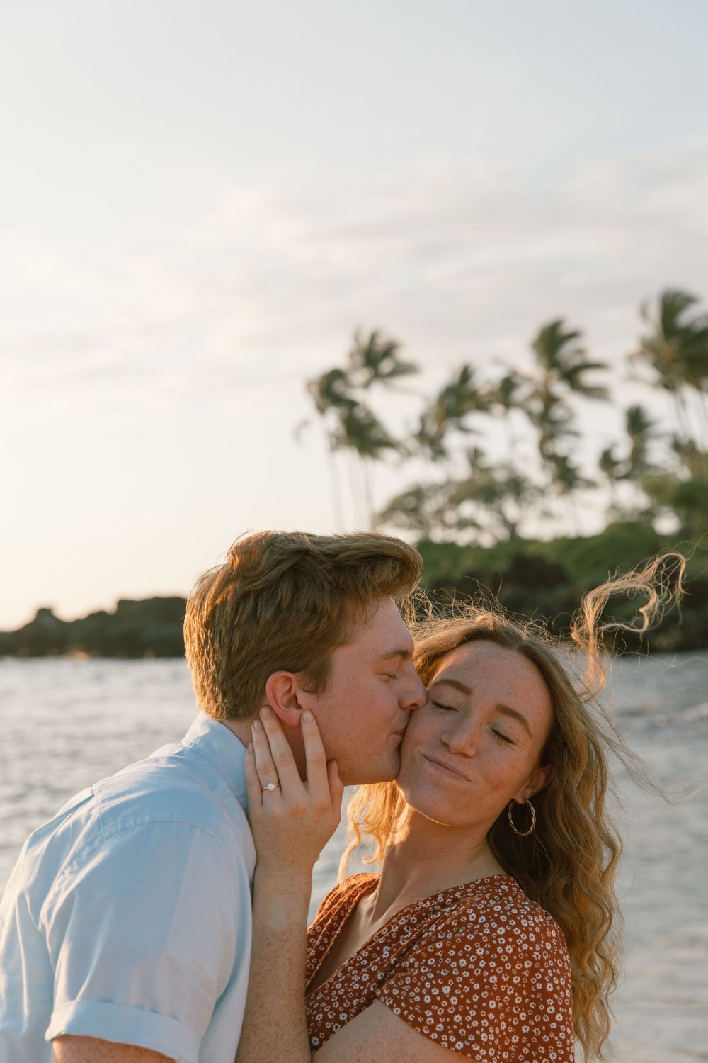 Sunset beach portrait with couple sharing an intimate kiss against palm tree backdrop.