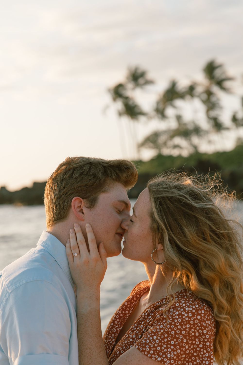 A couple shares a romantic kiss on a tropical beach at sunset.