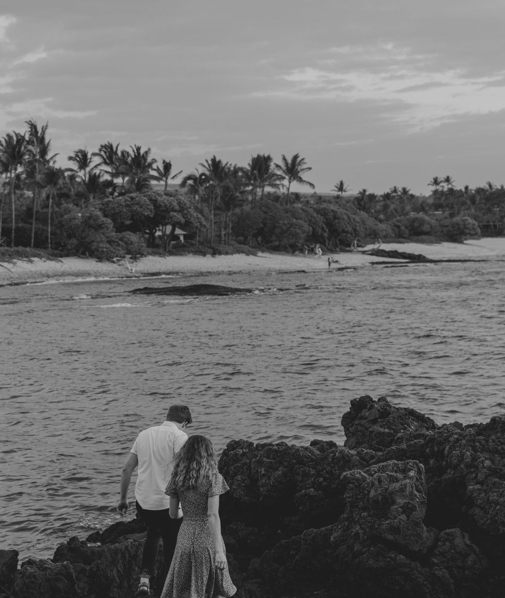 Couple standing on volcanic rocks overlooking the ocean at a Hawaiian beach.