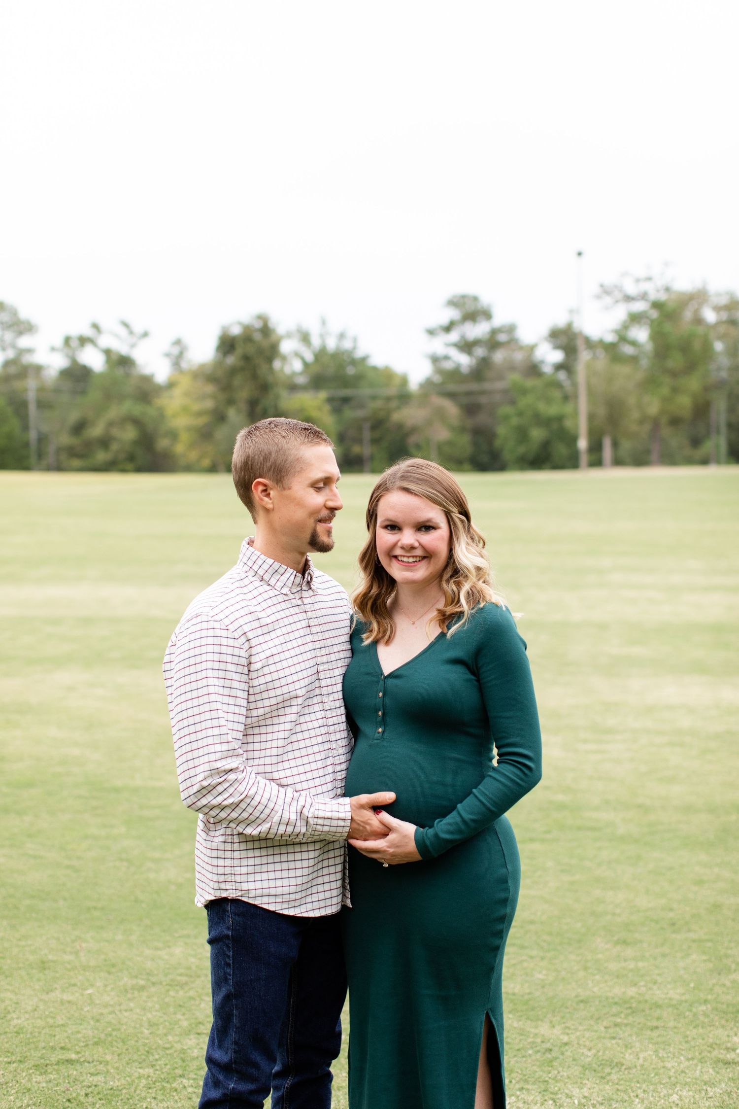 Joyful maternity portrait in an open field with couple in coordinated casual wear.