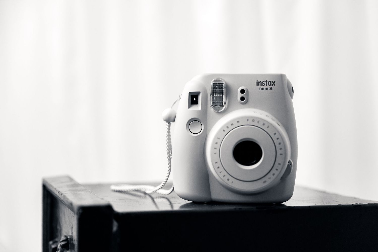 White Fujifilm Instax Mini instant camera on dark surface in monochrome style.