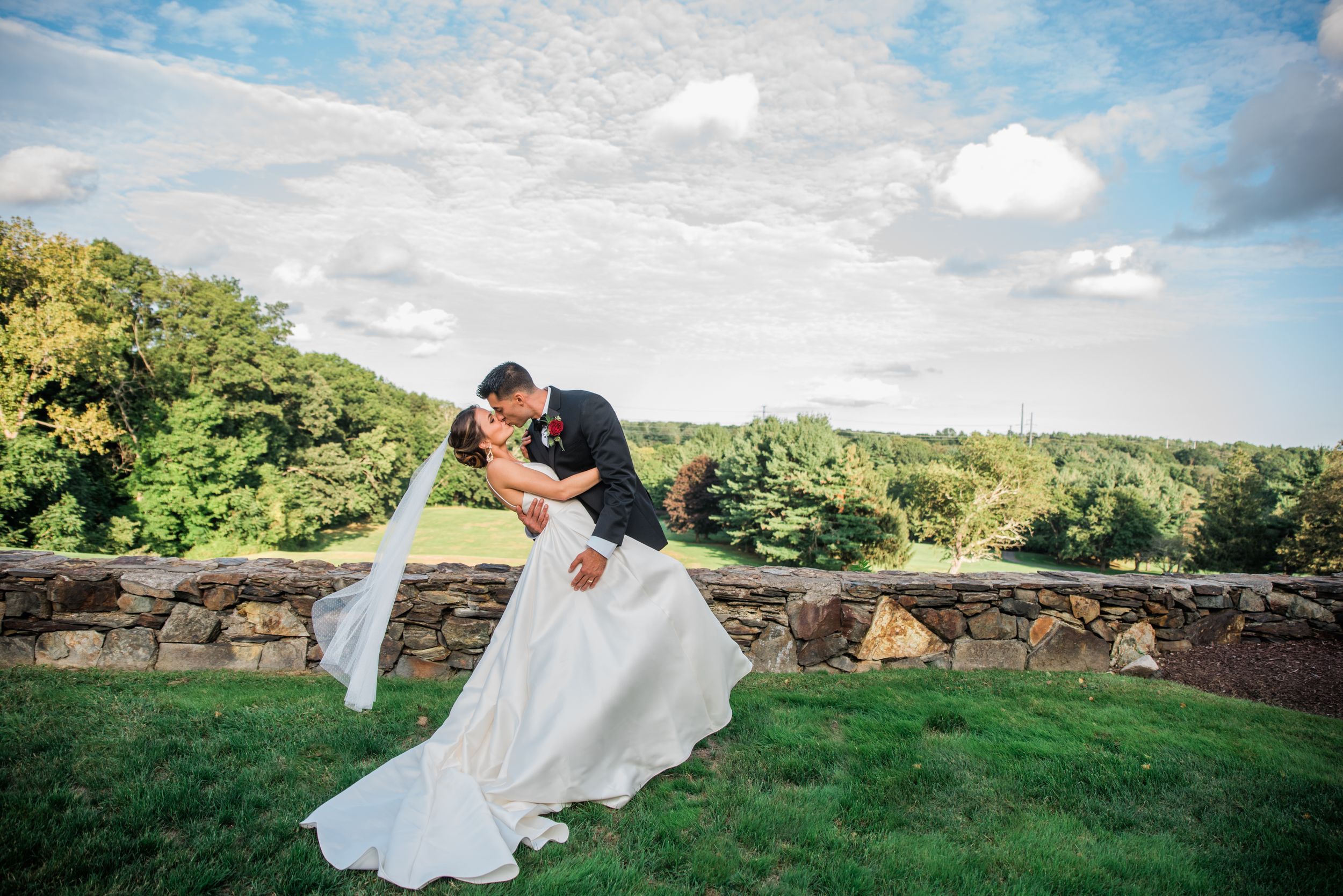 A classic dip pose wedding photo on a scenic stone terrace overlooking green hills.