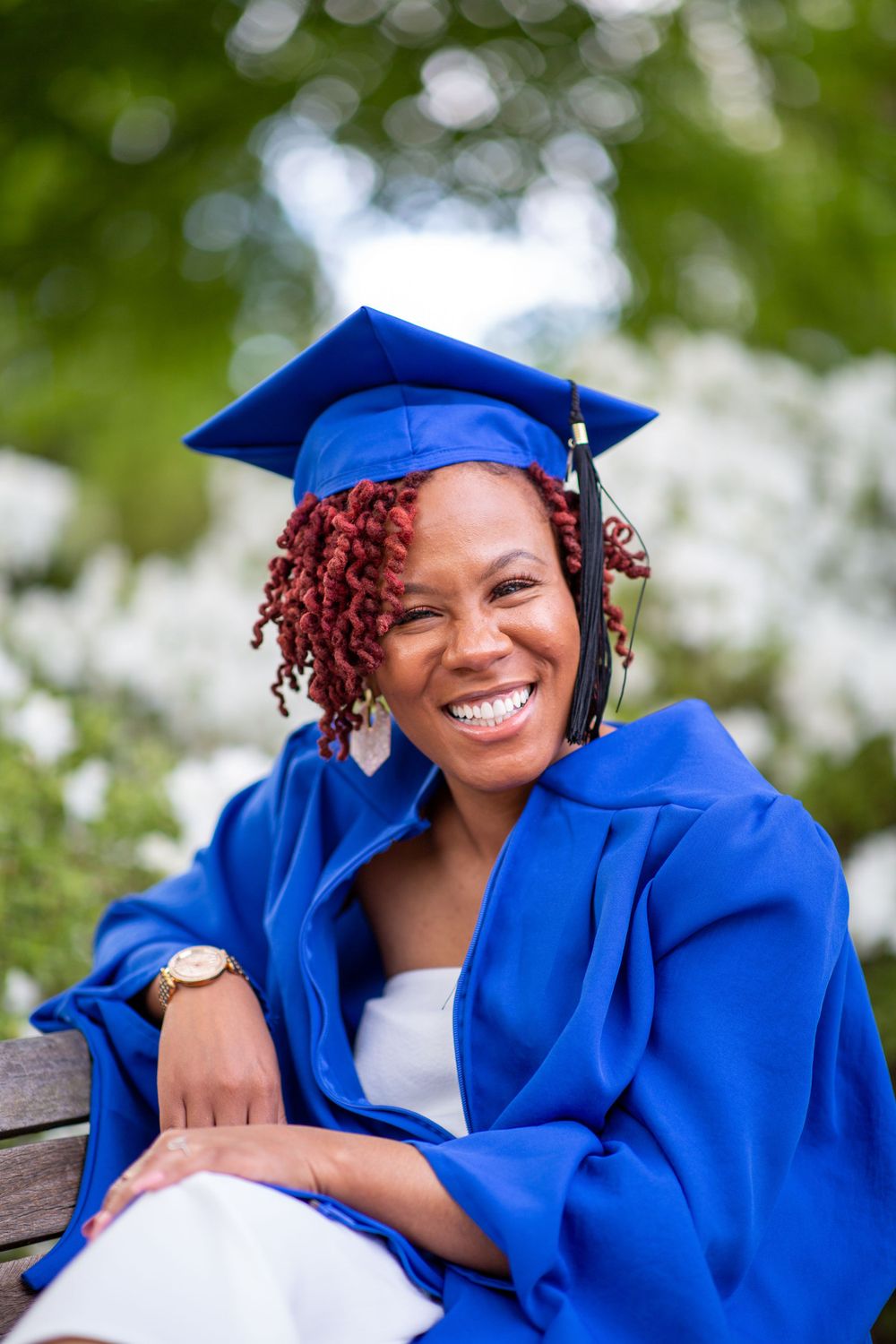 Graduation portrait in blue cap and gown outdoors with bokeh background.