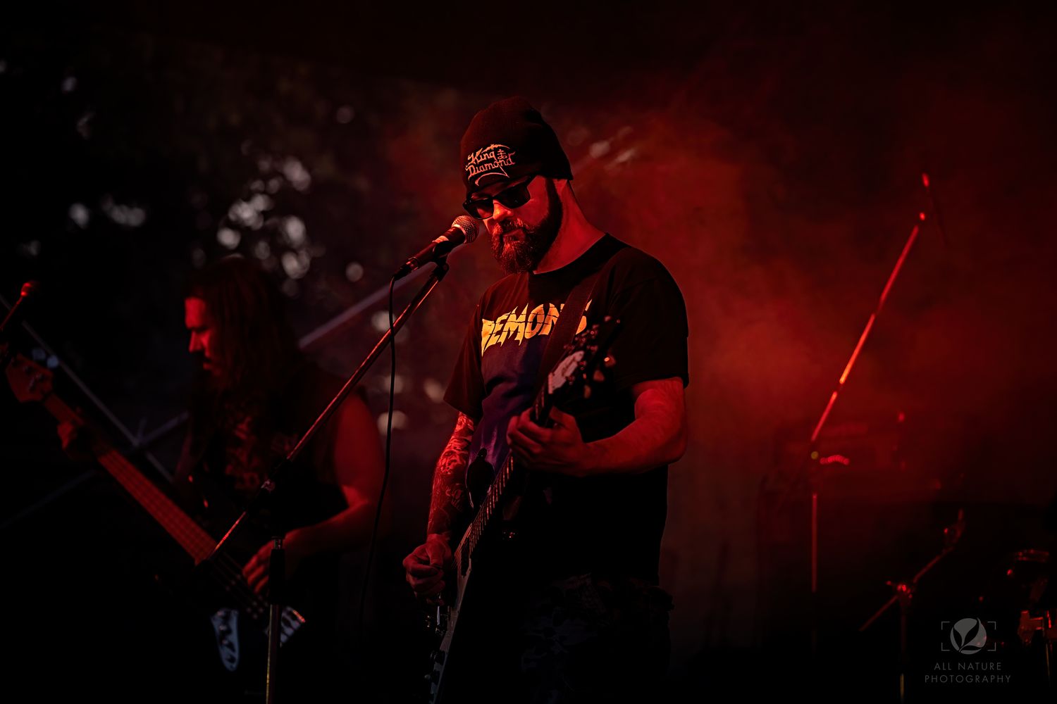 Performer singing into microphone on stage with dramatic red lighting.