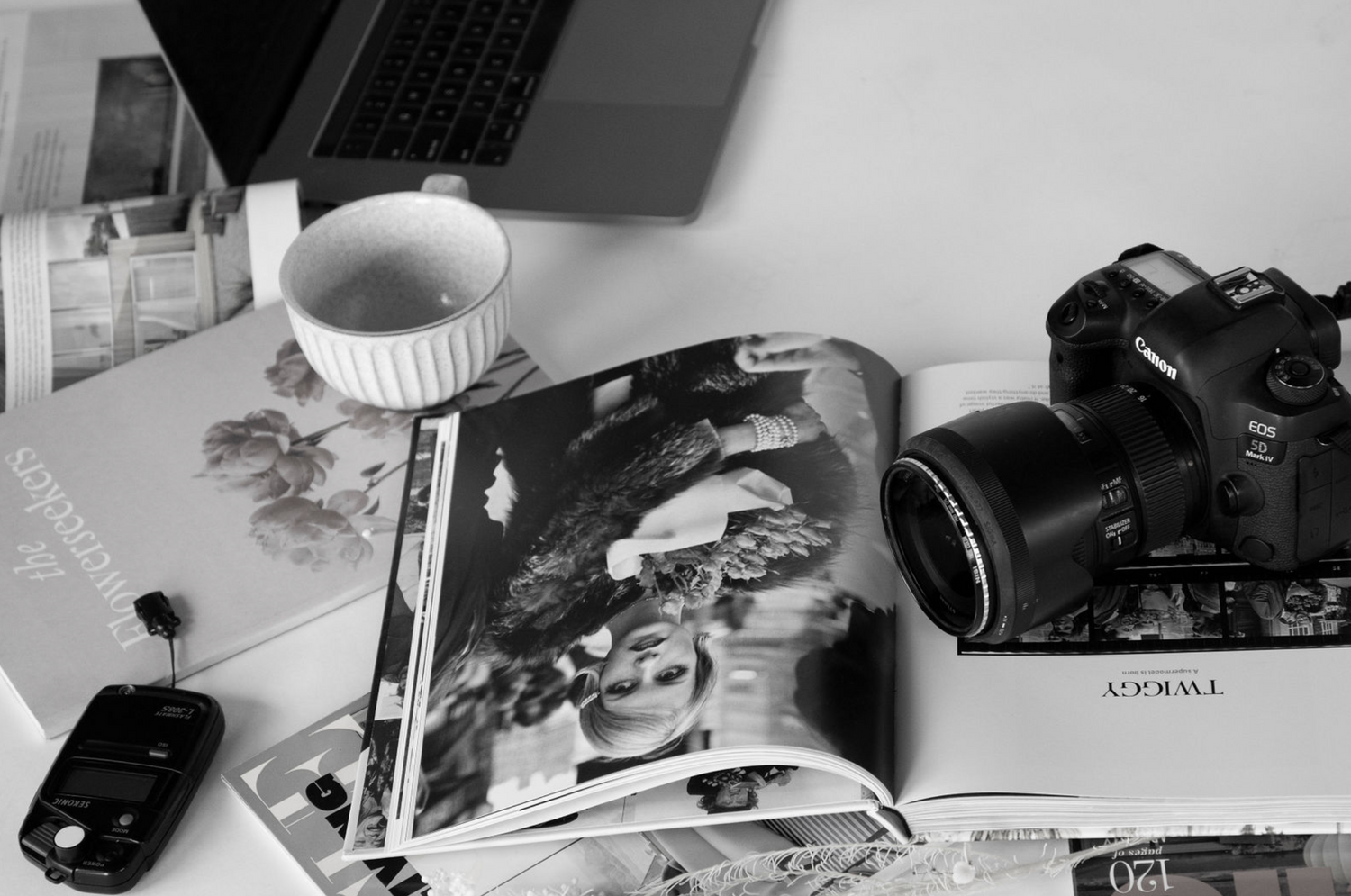 Black and white desk setup with camera, laptop, magazine and coffee cup.
