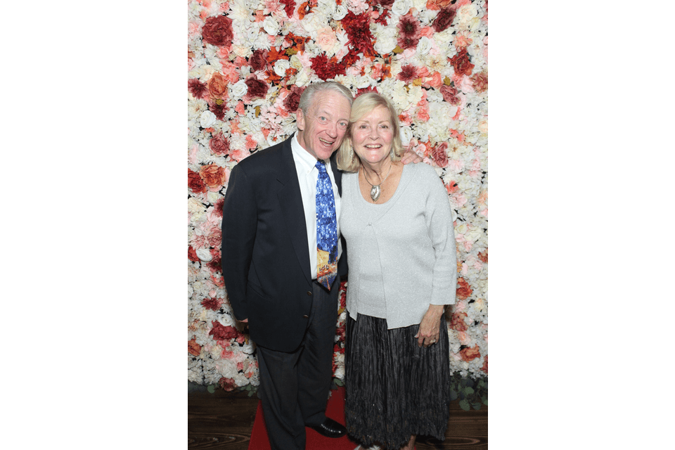 A couple poses together against a floral backdrop with red and pink roses.